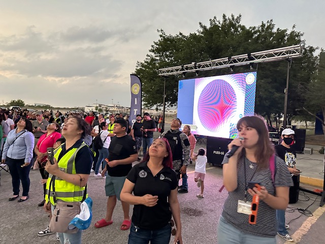 The same crowd of people looking up at the sky, which is still bright and cloudy