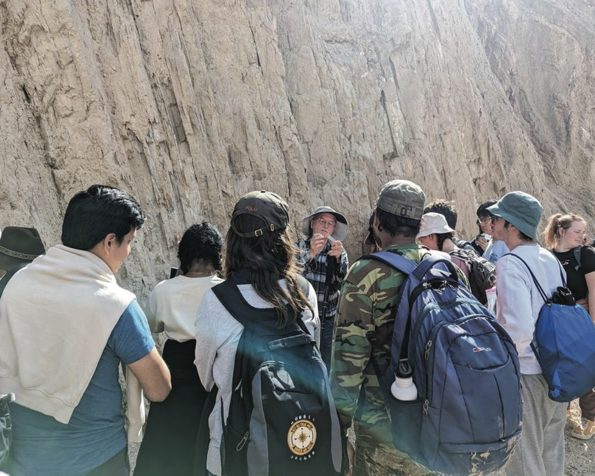 Students gathered around a cliff face, listening as someone speaks