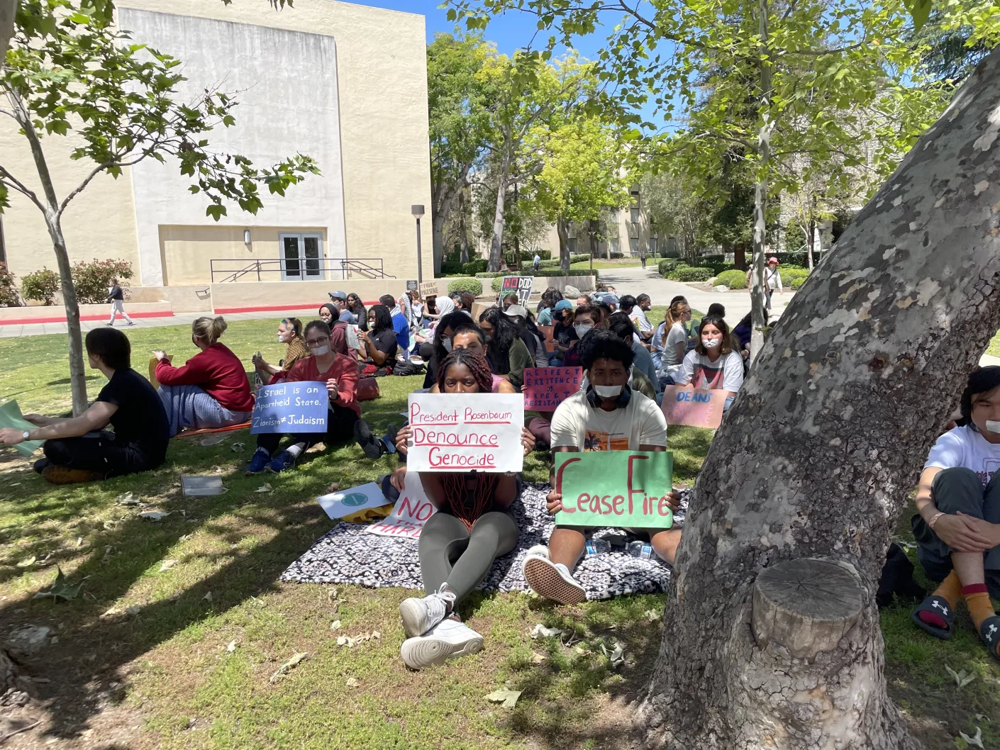 A group of protesters sitting outside Red Door with tape over their mouths, holding signs reading “President Rosenbaum: Denounce Genocide,” “CeaseFire,” and more