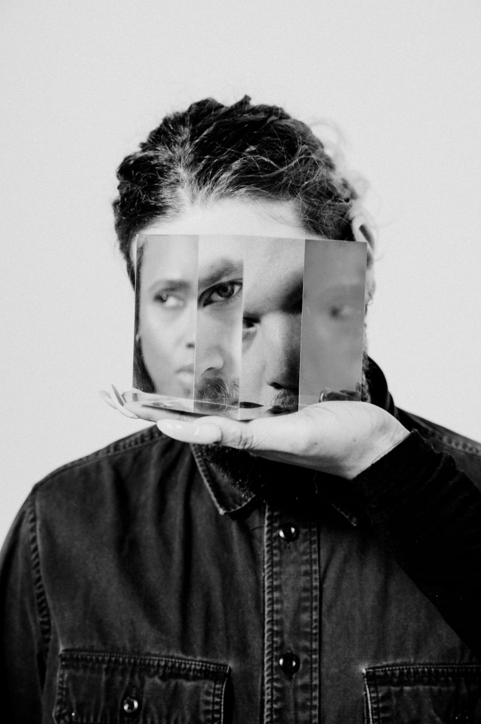 Photo of someone holding a translucent cube in front of their face, so multiple different faces appear as facets in the cube.